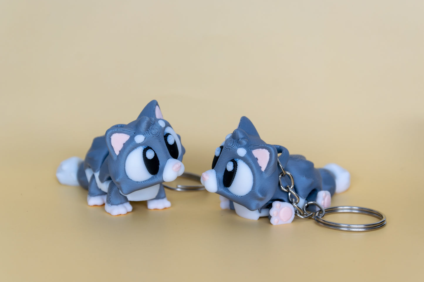 Deux exemplaires du porte-clés Chat articulé MinoZoo gris doux et crème, en vue trois quarts face à face.