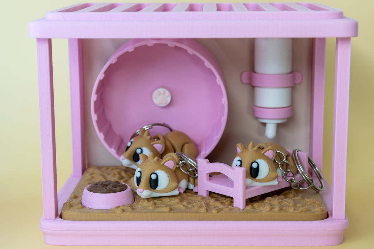 Plusieurs porte-clés Hamster articulés MinoZoo brun, blanc et rose, vue de face dans un décor rose.