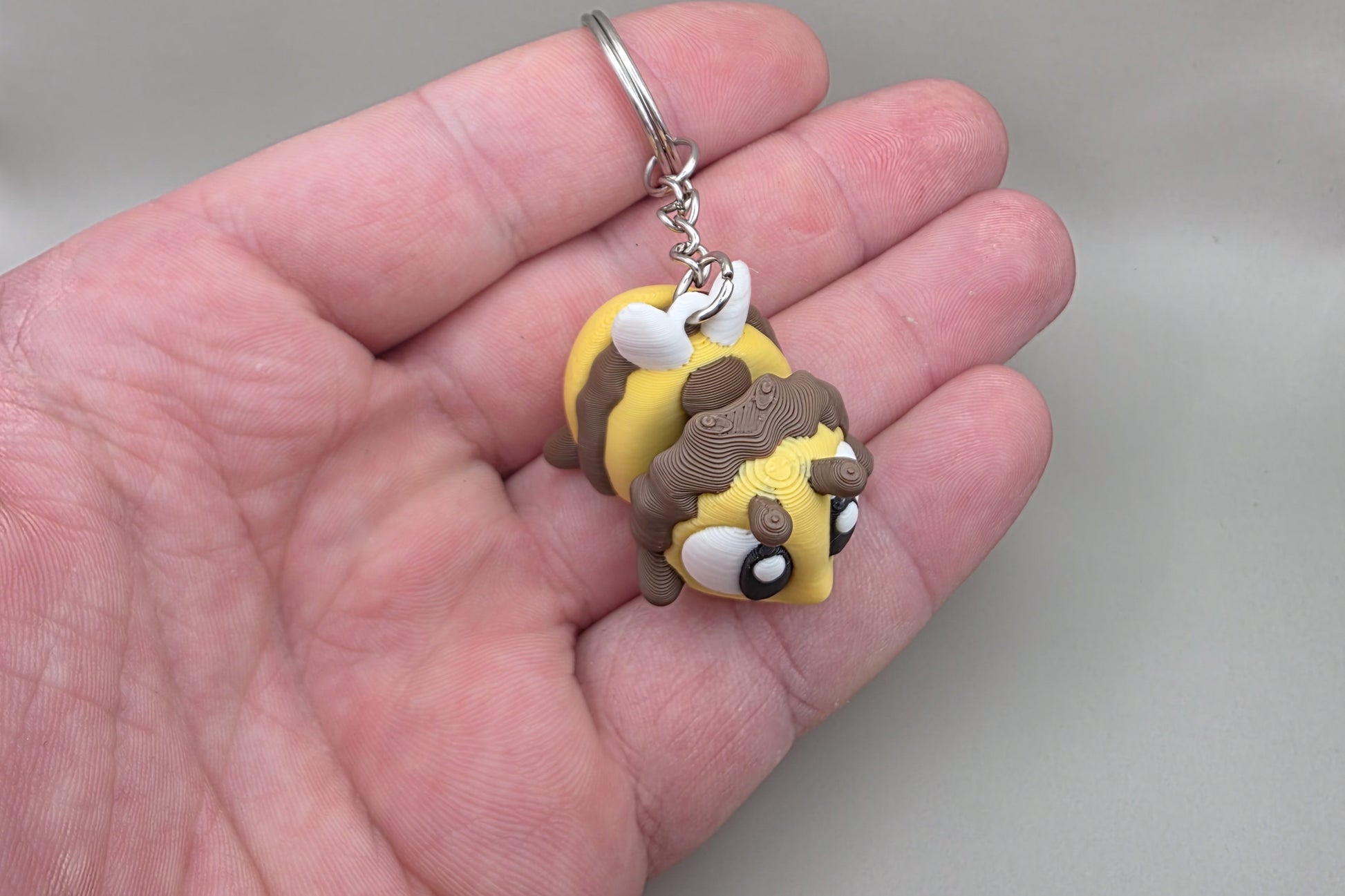 Porte-clés Abeille articulé MinoZoo jaune, brun et blanc, vu de dessus dans une main.