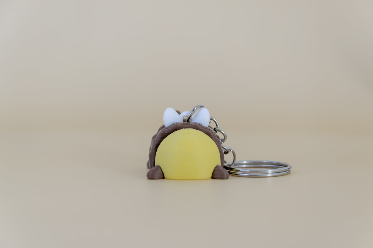 Porte-clés Abeille articulé MinoZoo jaune, brun et blanc, vue de dos avec anneau sur fond beige.