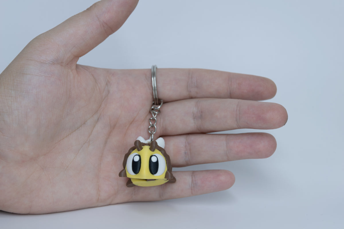 Porte-clés Abeille articulé MinoZoo jaune, brun et blanc, vue de face tenu dans une main.