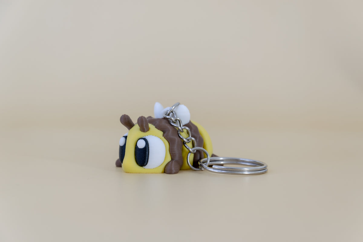 Porte-clés Abeille articulé MinoZoo jaune, brun et blanc, vue trois-quarts avec anneau sur fond beige.