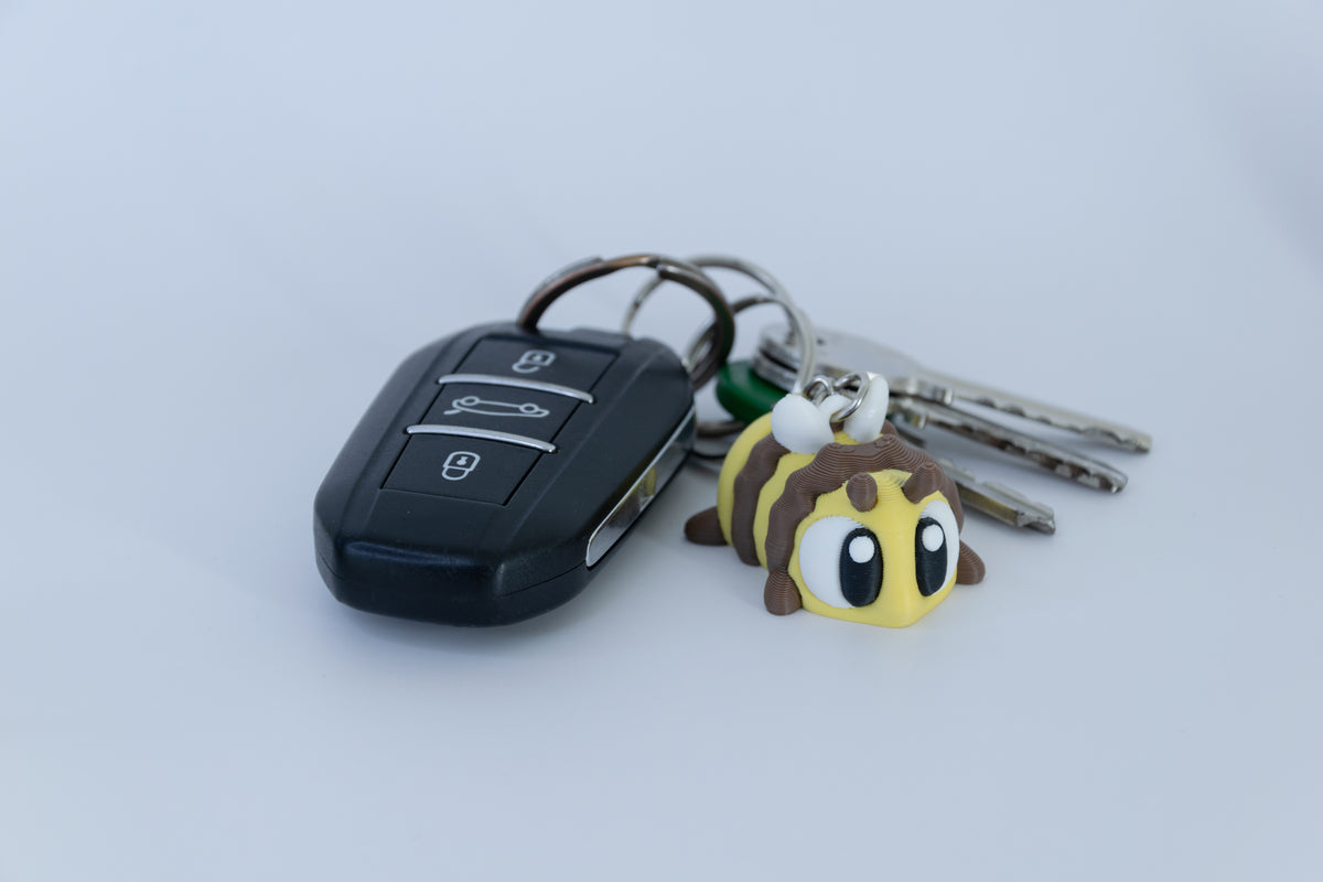 Porte-clés Abeille articulé MinoZoo jaune et brun, vue trois-quarts près de clés de voiture.