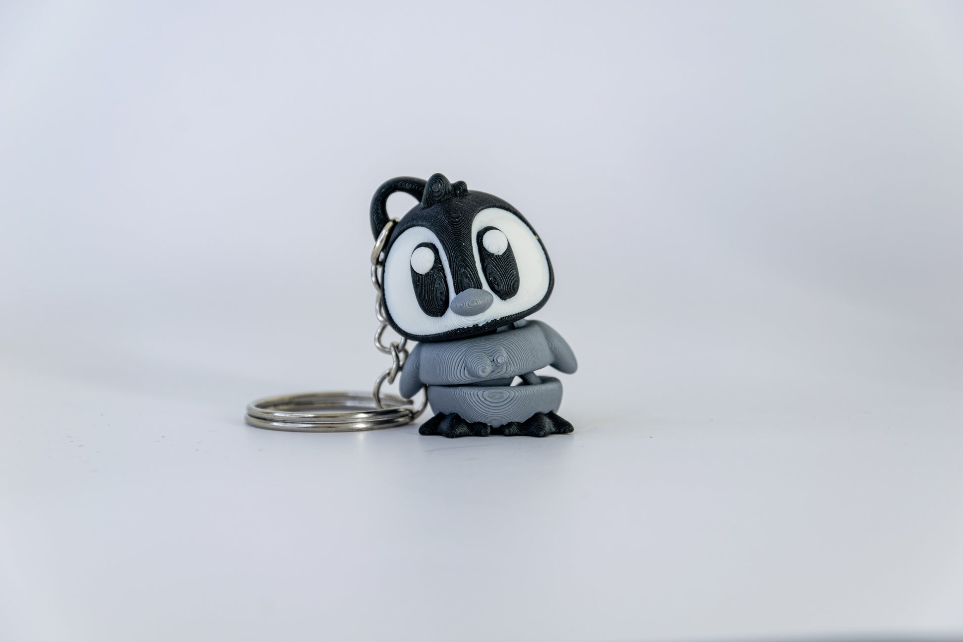 Porte-clés Bébé Pingouin articulé MinoZoo noir, blanc et gris moyen, posé de trois quarts sur fond blanc.