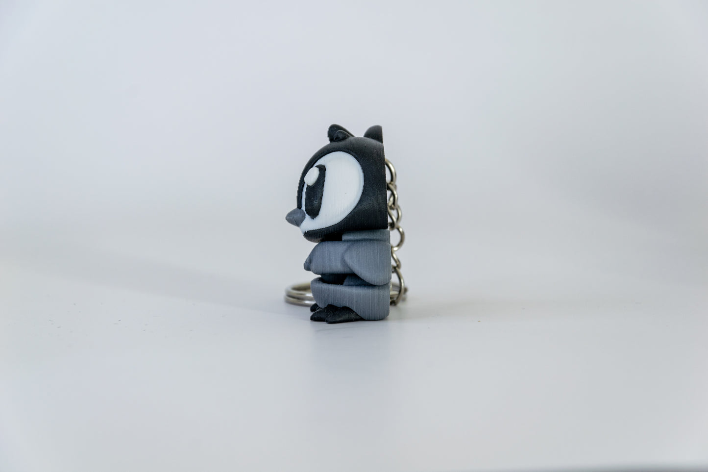 Porte-clés Bébé Pingouin articulé MinoZoo noir, blanc et gris moyen, vu de profil gauche avec chaîne derrière.