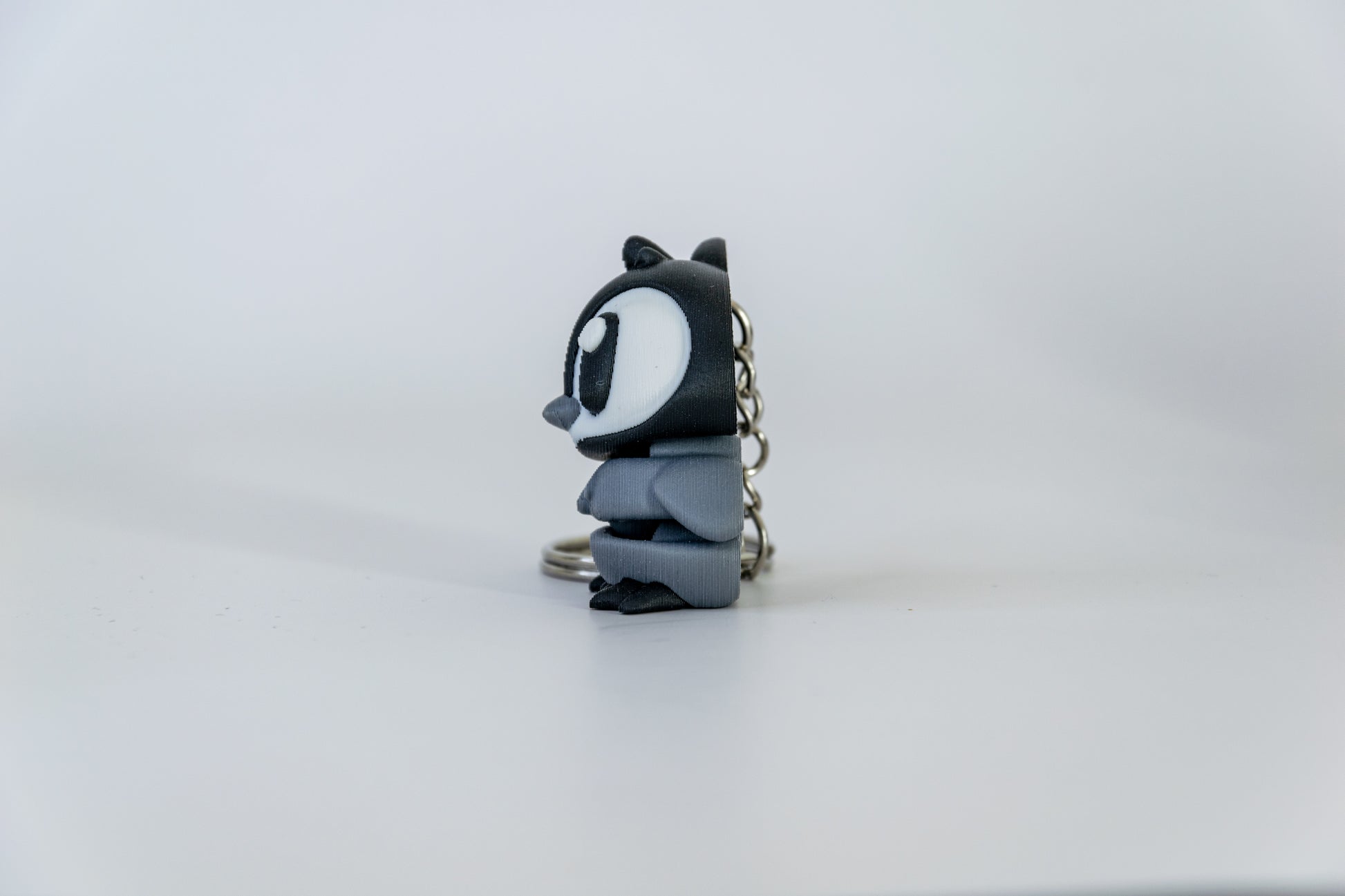 Porte-clés Bébé Pingouin articulé MinoZoo noir, blanc et gris moyen, vu de profil gauche avec chaîne derrière.