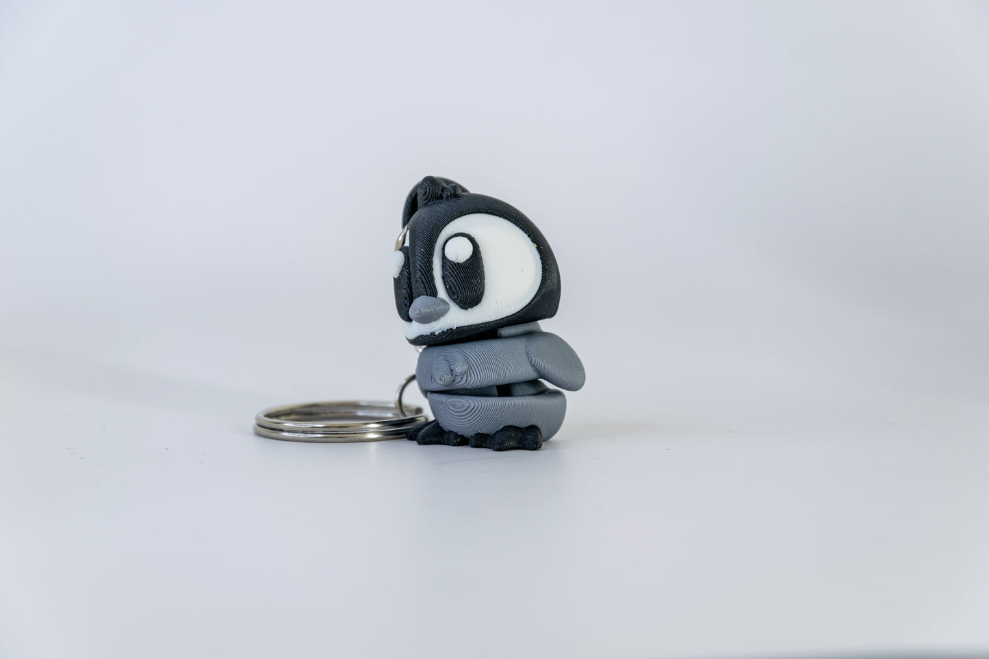 Porte-clés Bébé Pingouin articulé MinoZoo noir, blanc et gris moyen, vu de trois quarts gauche sur fond blanc.
