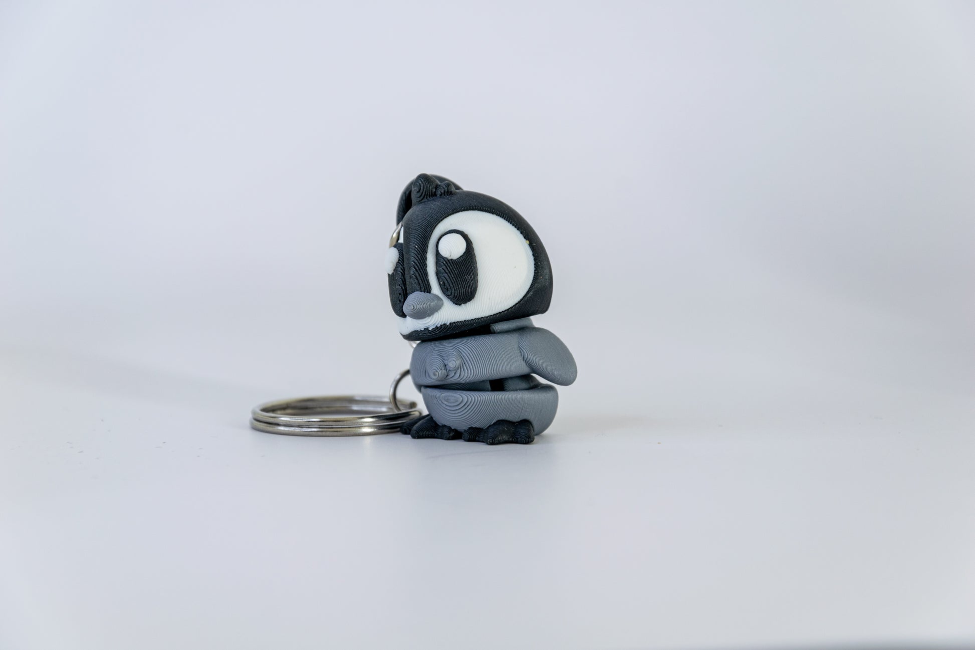 Porte-clés Bébé Pingouin articulé MinoZoo noir, blanc et gris moyen, vu de trois quarts gauche sur fond blanc.