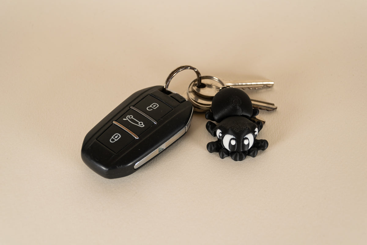 Porte-clés Black Spider articulé MinoZoo noir et blanc, vue de dessus avec des clés de voiture.