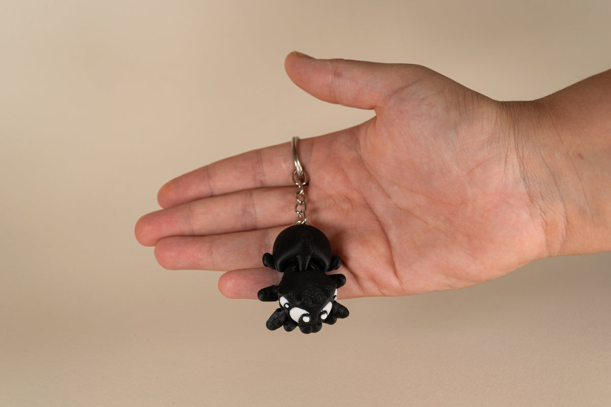 Porte-clés Black Spider articulé MinoZoo noir et blanc, vue de dessus tenu dans une main.