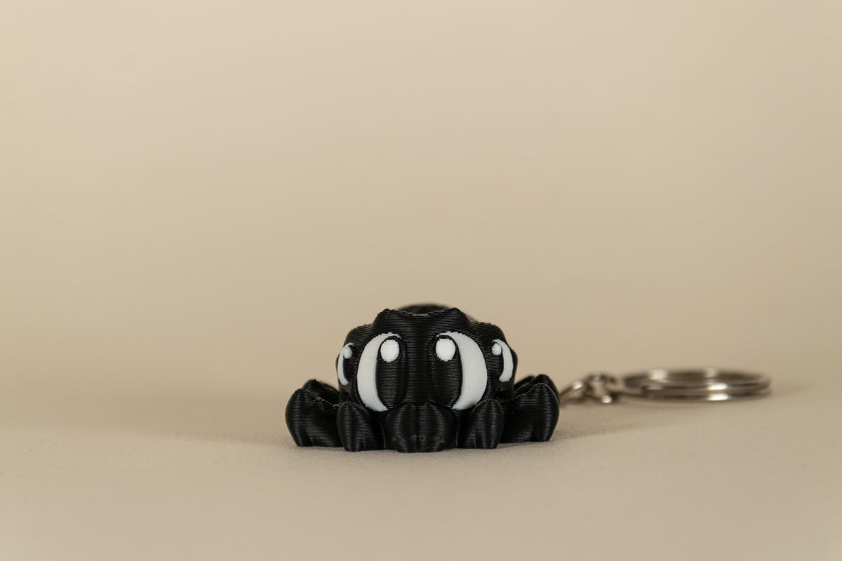 Porte-clés Black Spider articulé MinoZoo noir et blanc, vue de face sur fond beige.