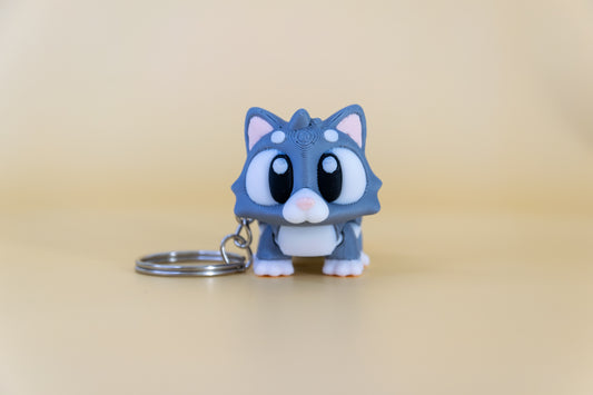 Porte-clés Chat articulé MinoZoo gris doux et crème, vue de face avec anneau posé sur fond beige.