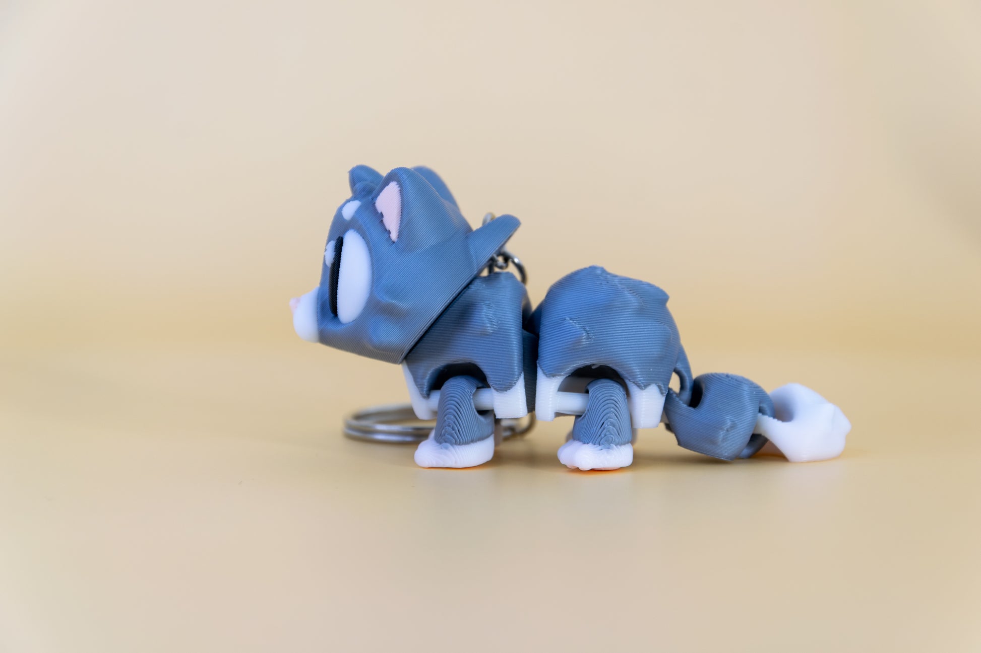 Porte-clés Chat articulé MinoZoo gris doux et crème, vue de profil montrant le corps segmenté et la queue.