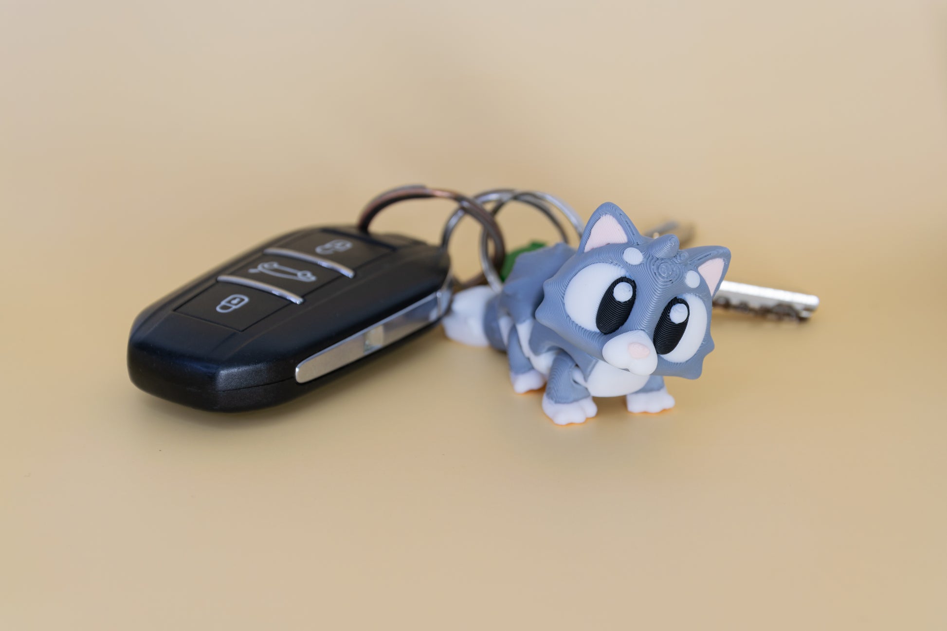 Porte-clés Chat articulé MinoZoo gris doux et crème, vue trois quarts à côté de clés de voiture.