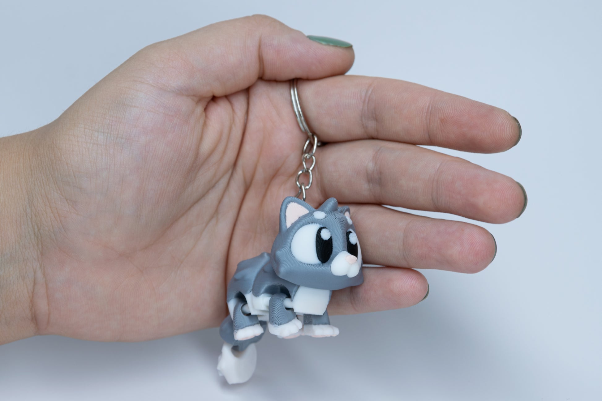 Porte-clés Chat articulé MinoZoo gris doux et crème, tenu dans une main en vue trois quarts.