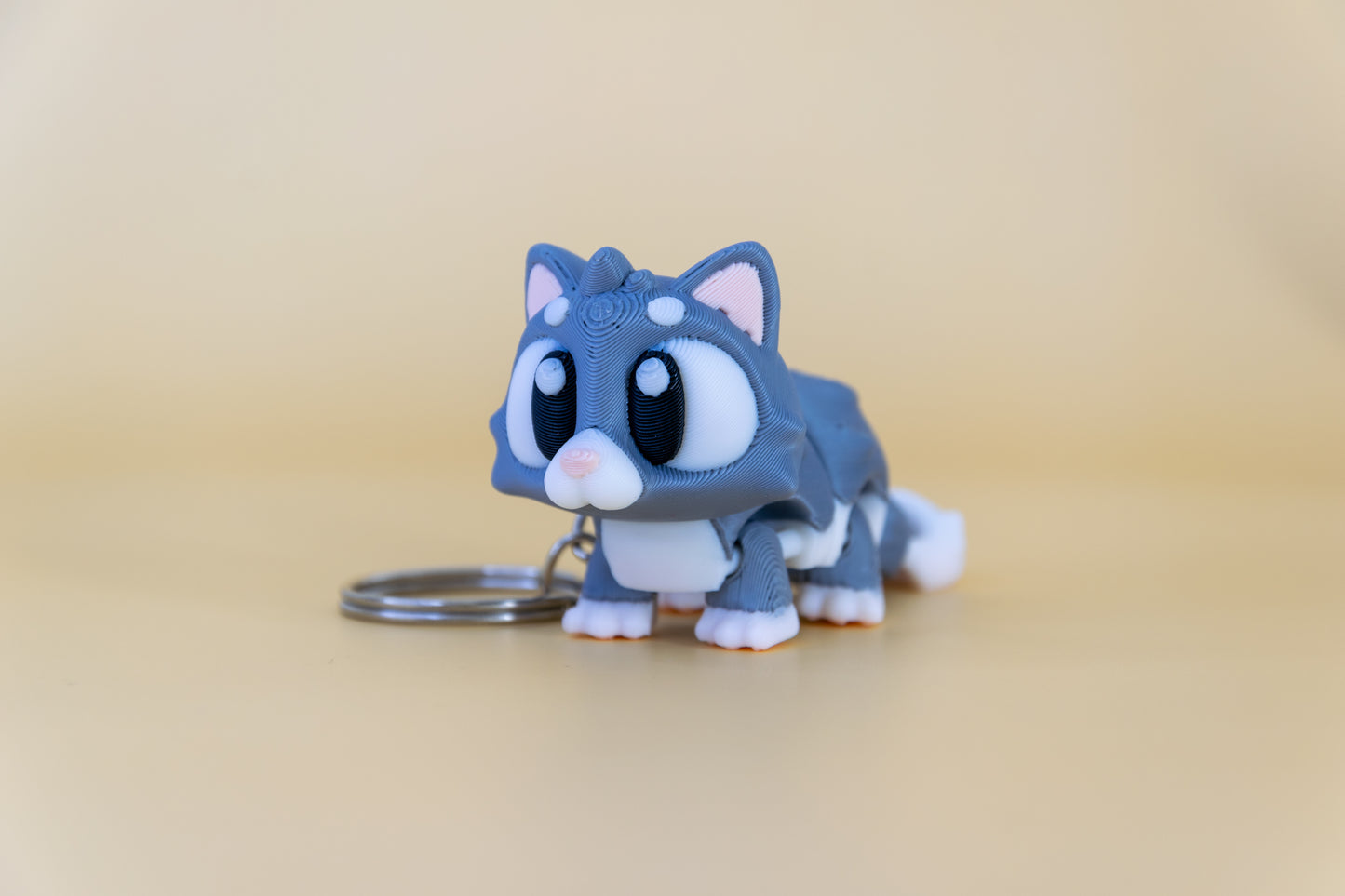 Porte-clés Chat articulé MinoZoo gris doux et crème, vue trois quarts avec anneau sur fond beige.