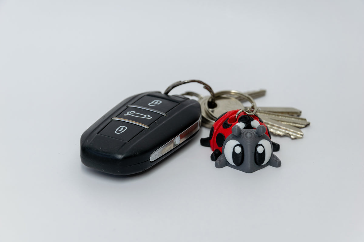 Porte-clés Coccinelle articulé MinoZoo rouge, gris foncé et noir, vue trois quarts avec des clés de voiture.