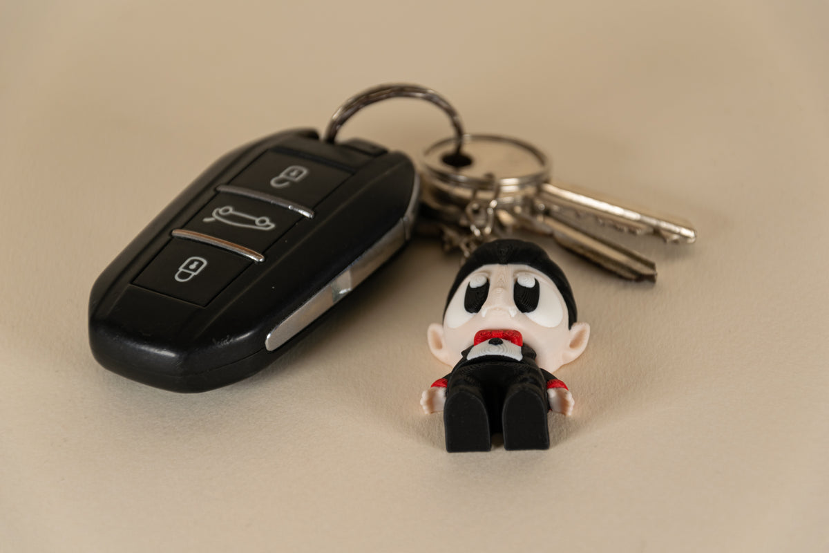 Porte-clés Dracula articulé MinoZoo noir, beige et rouge, vue de dessus avec des clés de voiture.