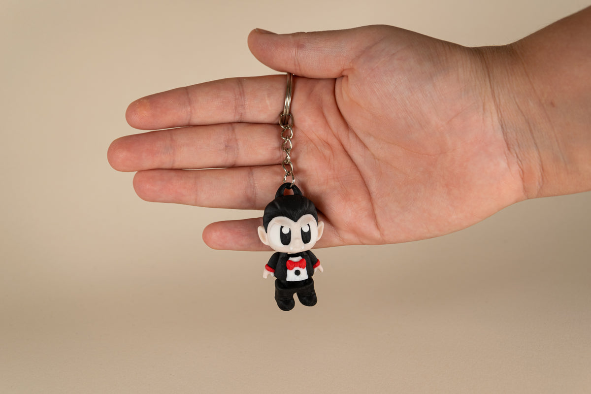 Porte-clés Dracula articulé MinoZoo noir, beige et rouge, vue de face tenu dans une main.