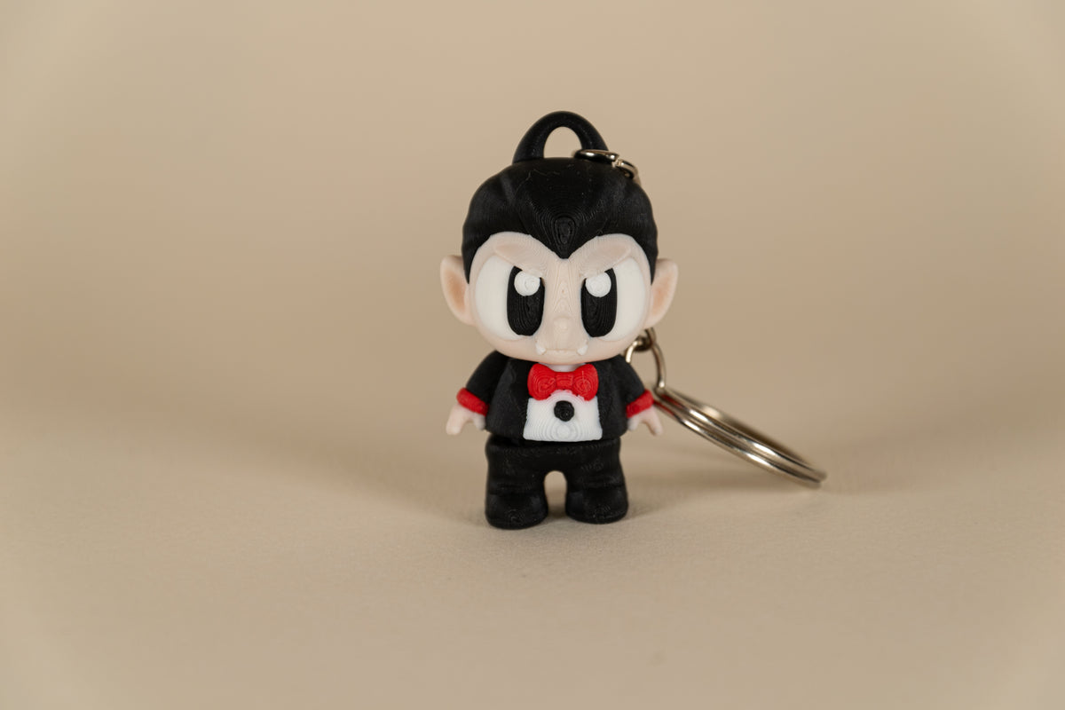 Porte-clés Dracula articulé MinoZoo noir, beige et rouge, vue de face sur fond beige.