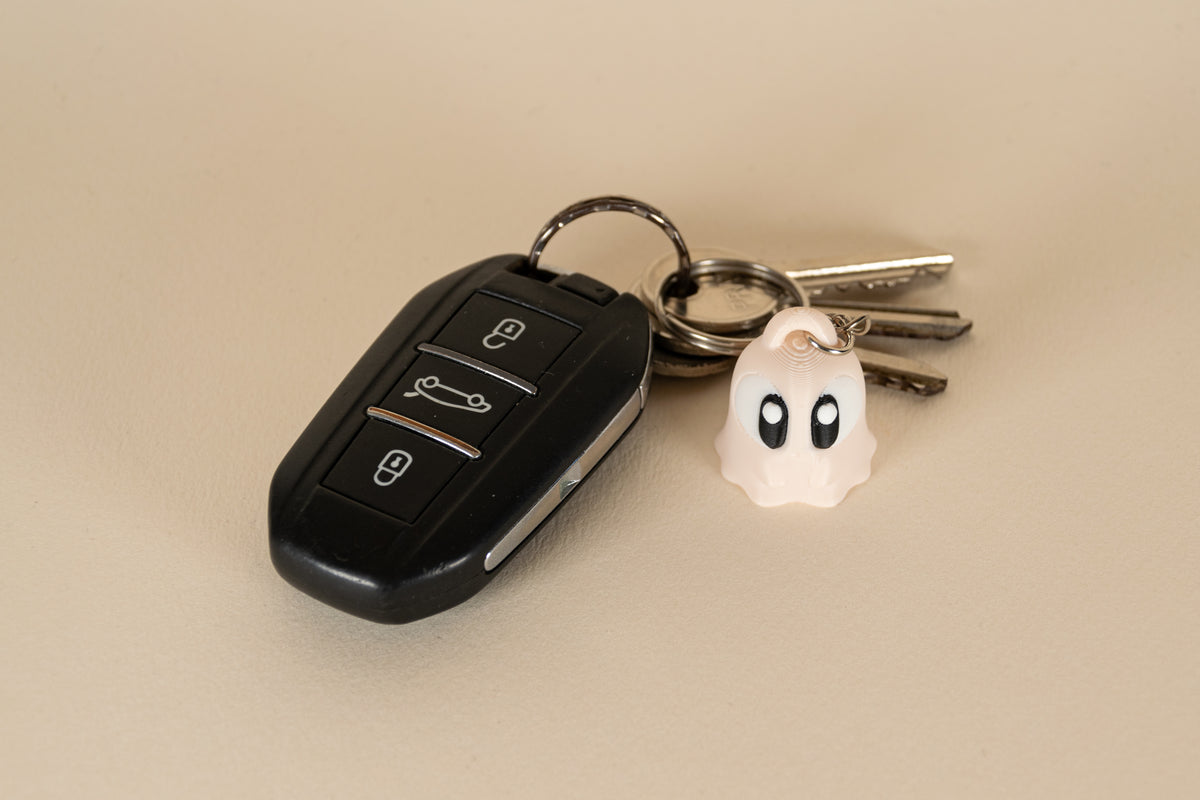 Porte-clés Ghost MinoZoo beige, noir et blanc, vue de face avec des clés de voiture.
