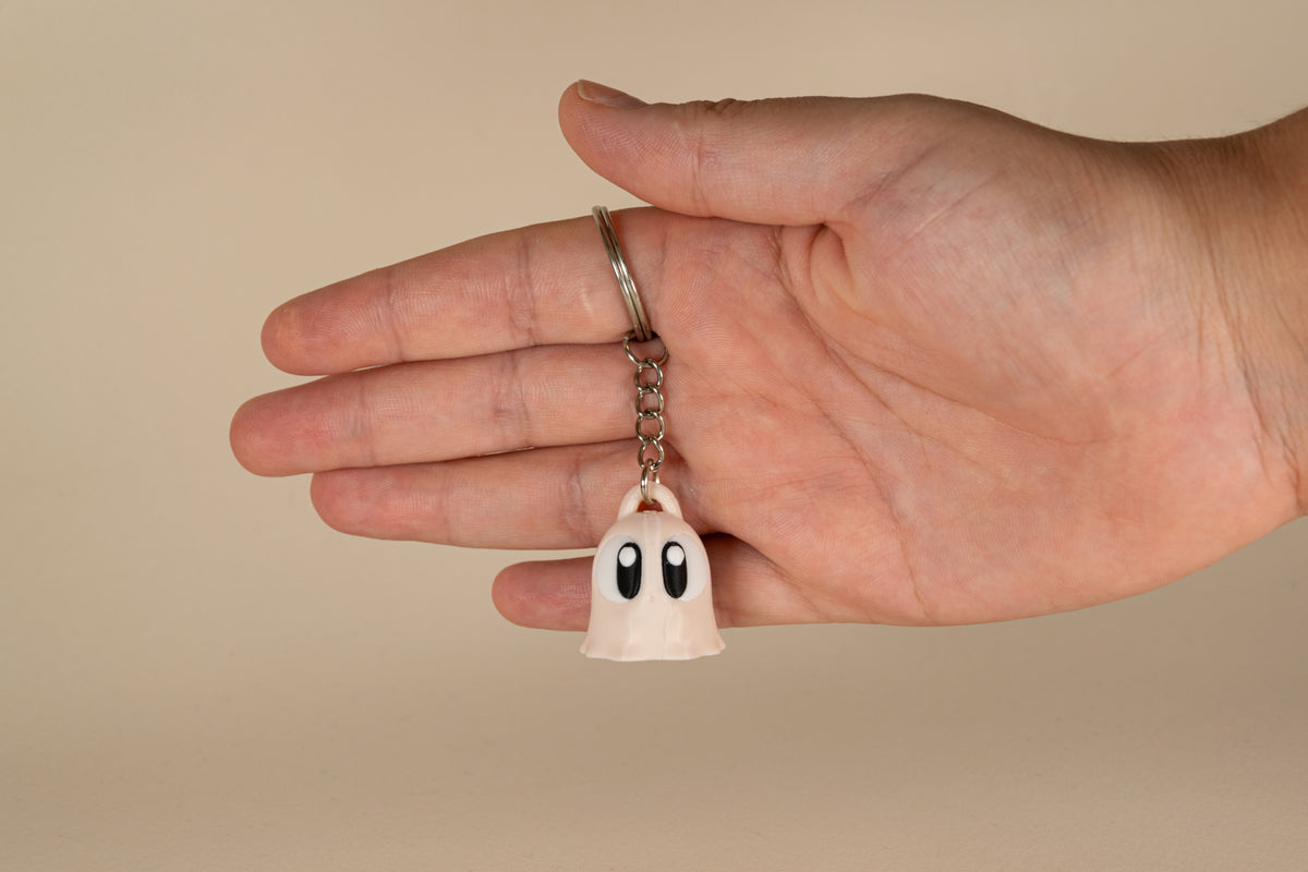 Porte-clés Ghost MinoZoo beige, noir et blanc, vue de face tenu dans une main.