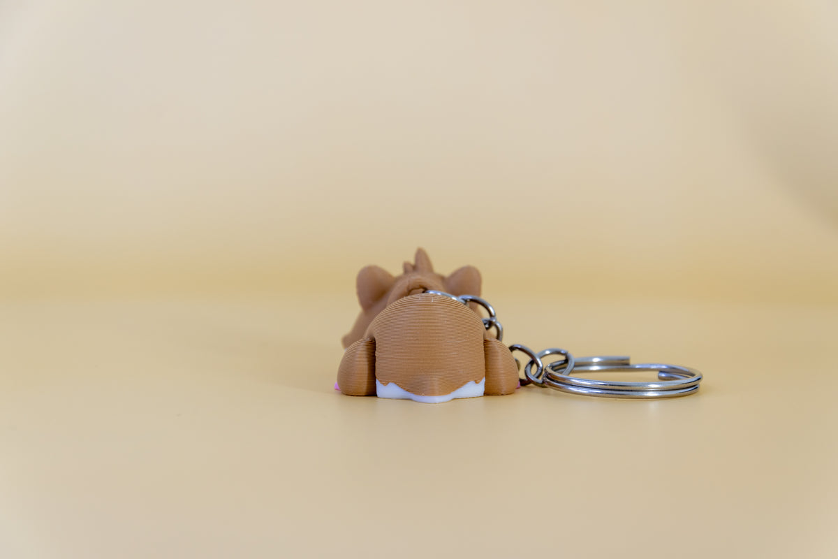 Porte-clés Hamster articulé MinoZoo brun et blanc, vue de dos sur fond beige.