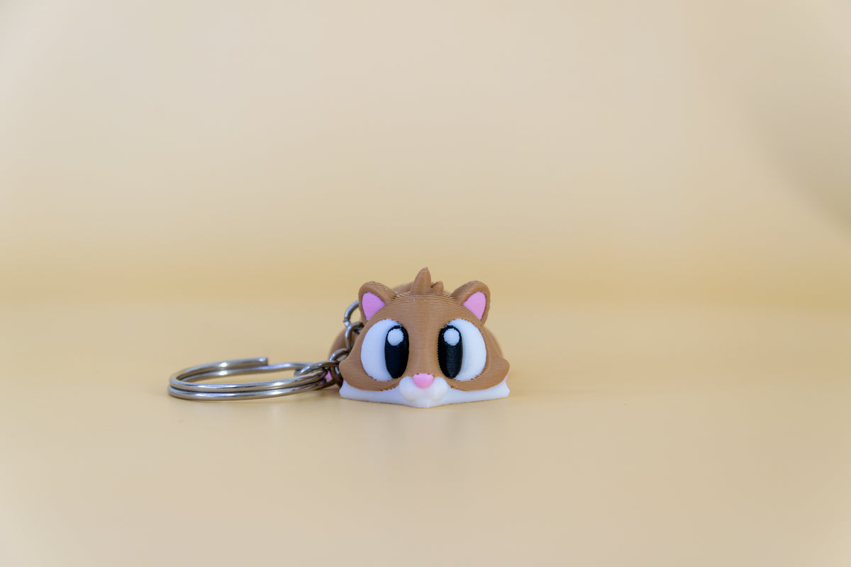 Porte-clés Hamster articulé MinoZoo brun, blanc et rose, vue de face sur fond beige.