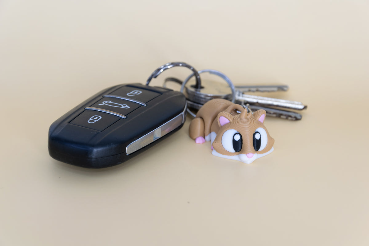 Porte-clés Hamster articulé MinoZoo brun, blanc et rose, vue trois-quarts près de clés de voiture.