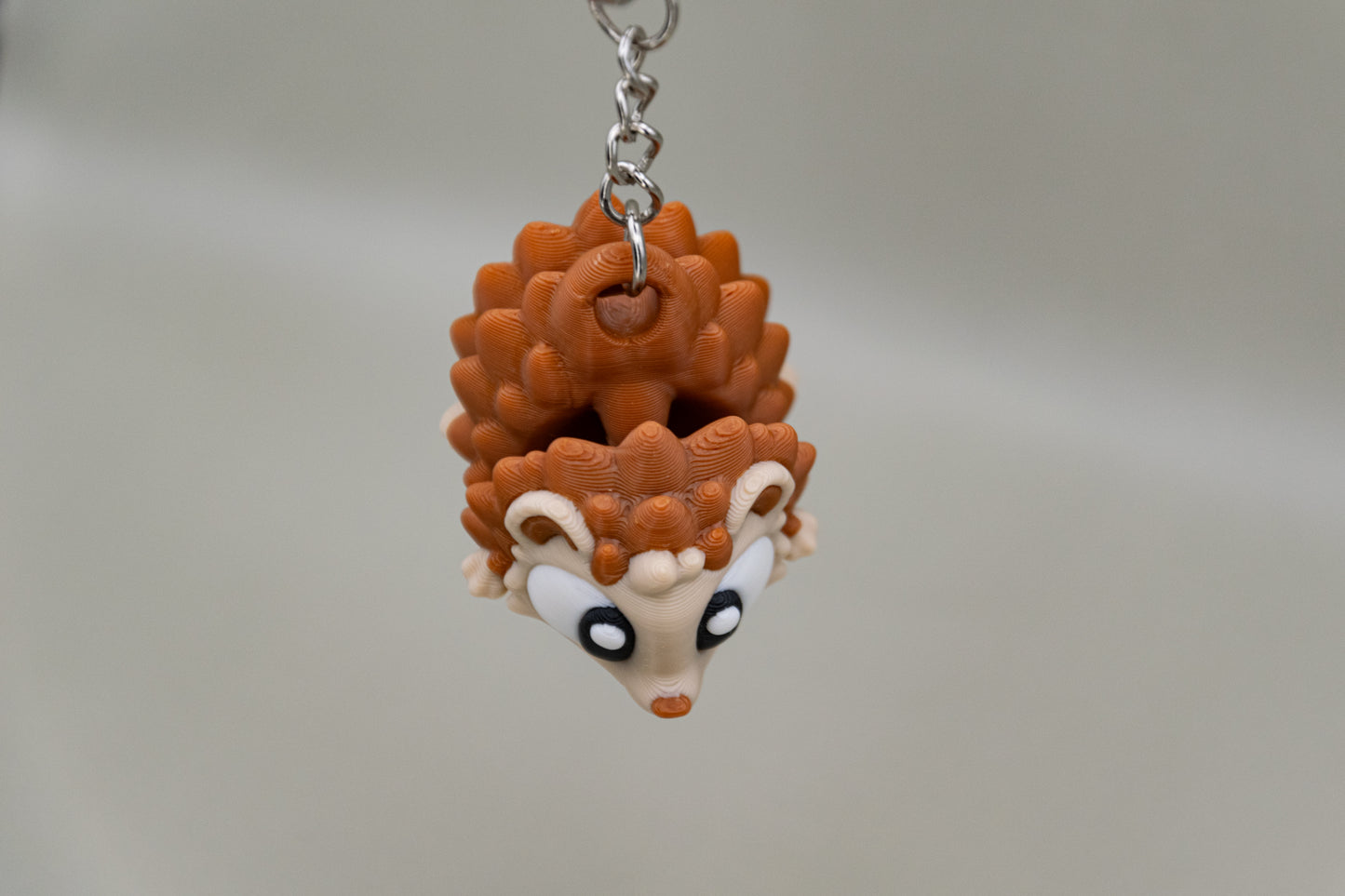 Porte-clés Hérisson articulé MinoZoo beige et brun caramel, suspendu de face sur fond gris.