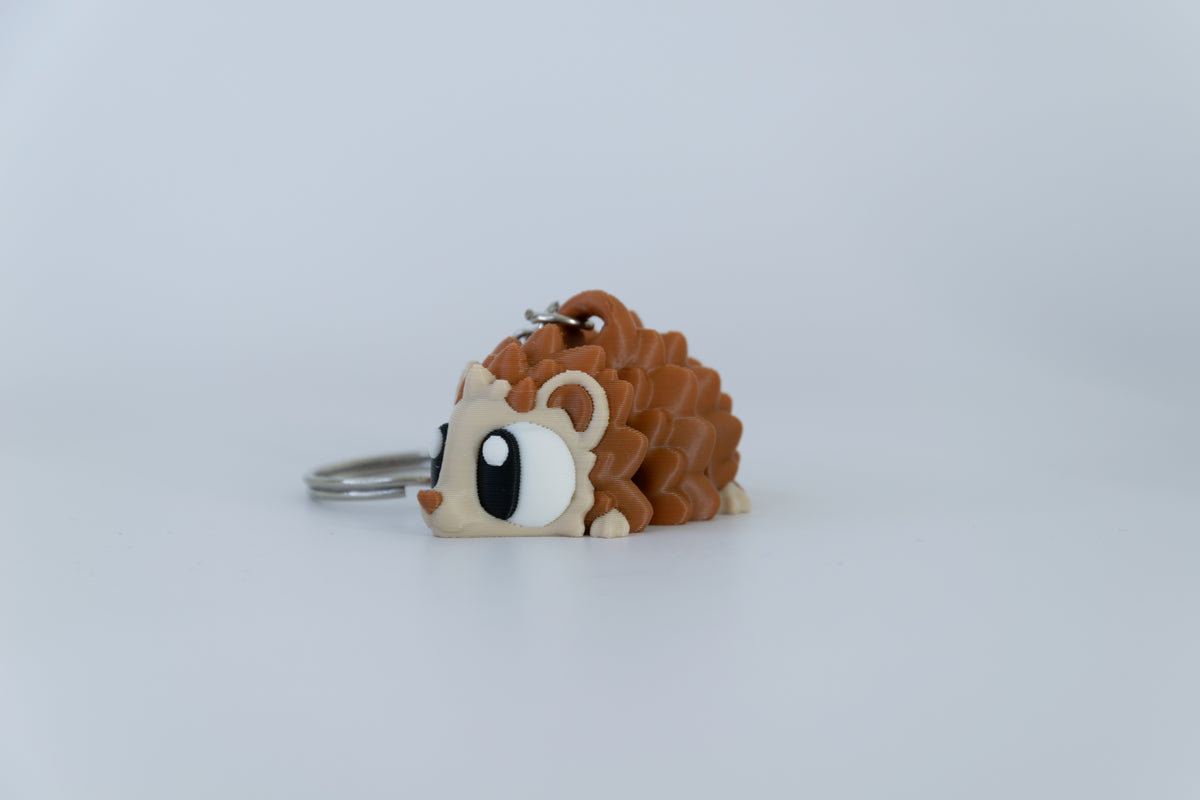Porte-clés Hérisson articulé MinoZoo brun et beige, posé de profil sur fond clair avec ses piquants en relief.