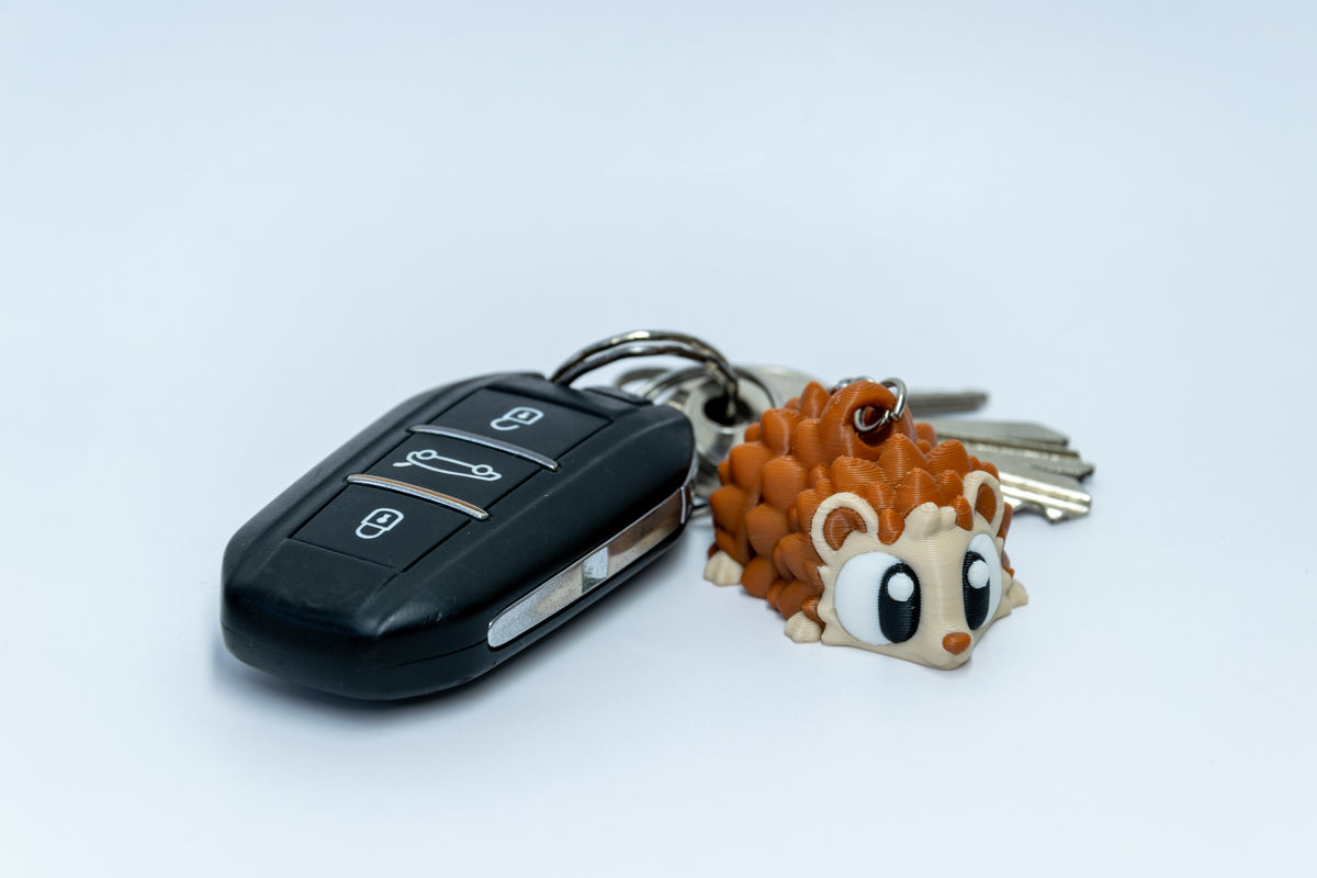 Porte-clés Hérisson articulé MinoZoo brun et beige, vue trois quarts à côté de clés de voiture.