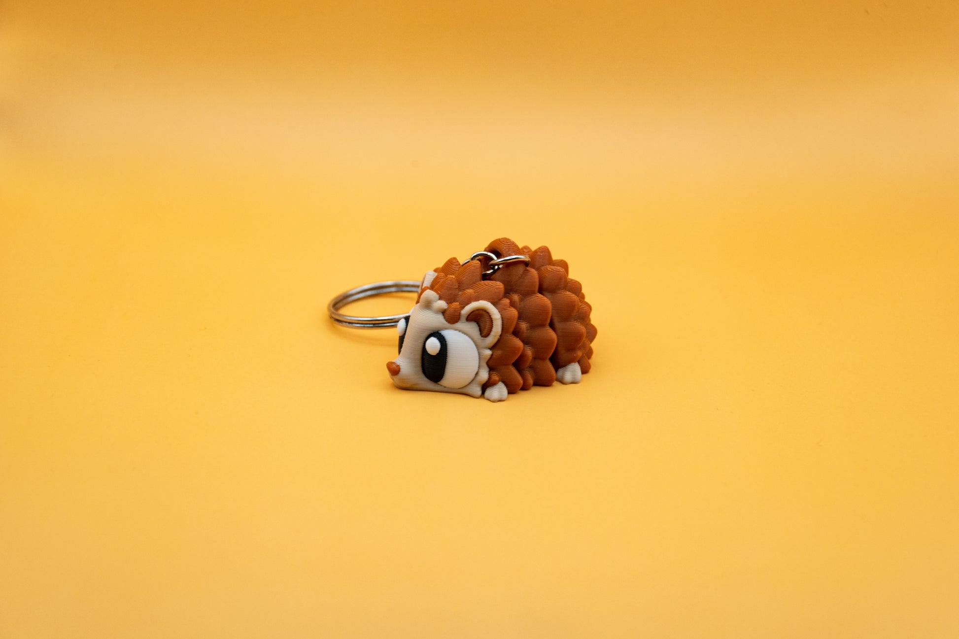 Porte-clés Hérisson articulé MinoZoo beige et brun caramel, posé de trois quarts sur fond orange.