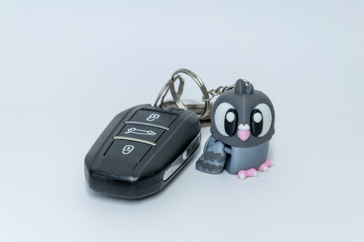 Porte-clés Pigeon articulé MinoZoo gris foncé, gris bleuté et rose, de trois quarts avec des clés de voiture.