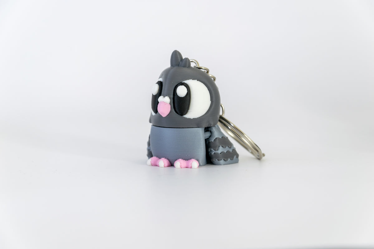 Porte-clés Pigeon articulé MinoZoo gris foncé, gris bleuté et rose, posé de trois quarts sur fond blanc.
